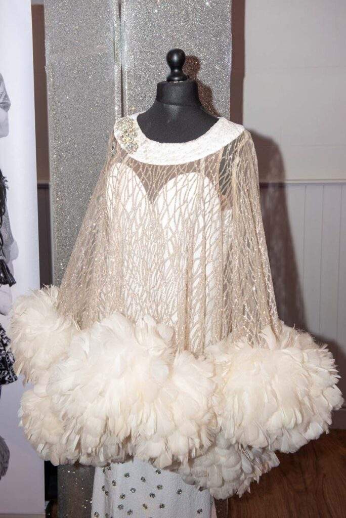 One of Ceri's beautiful costumes on a mannequin by the stage. It's a white full-length gown, under a sheer diamante laiden floaty top, the bottom of which is covered with white feathers.