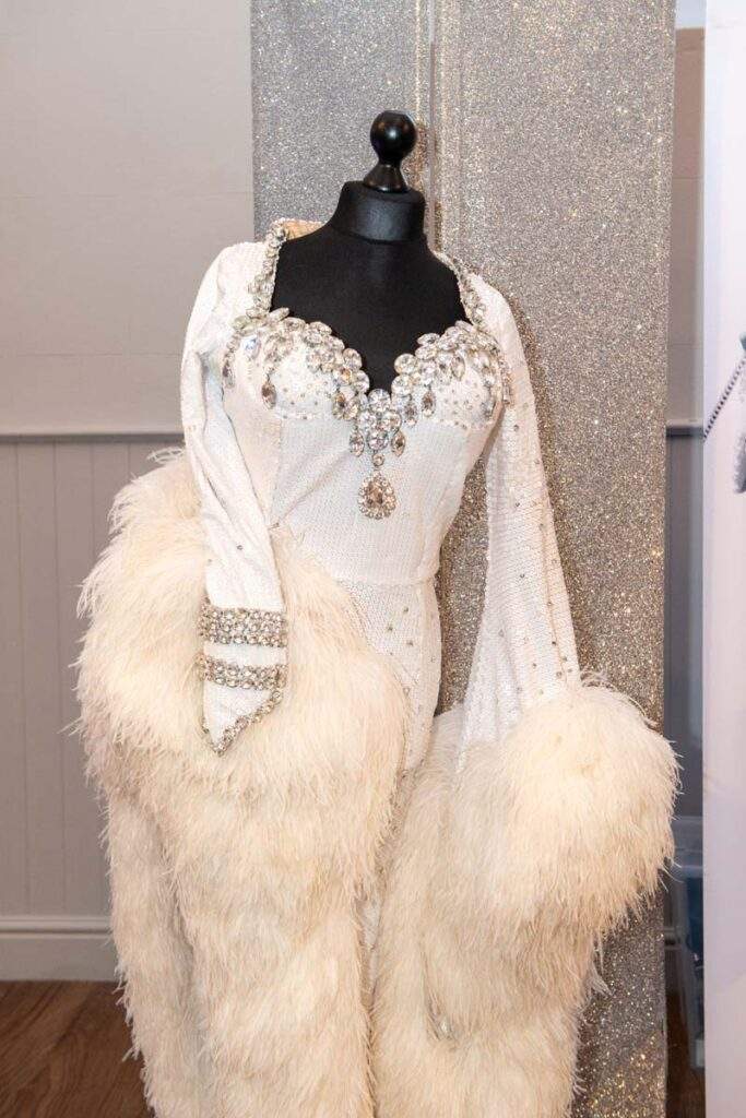 One of Ceri's beautiful costumes on a mannequin by the stage. It's a white full-length fitted gown, encrusted with diamantes around the heart neckline and left sleeve with lots of ostrich features around the sleeves