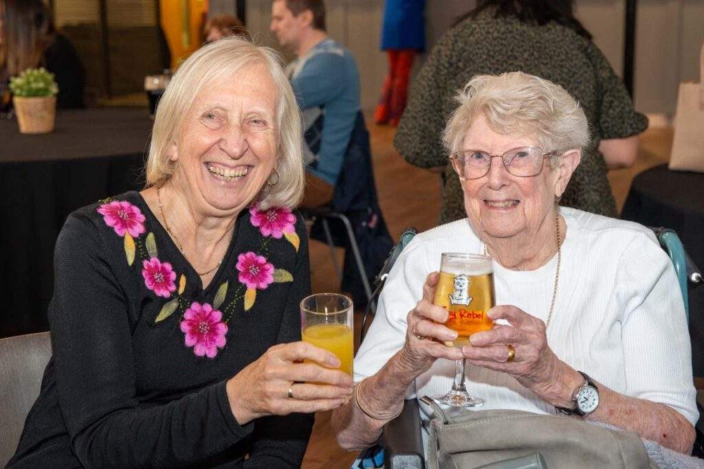Two women raising their drinks and smiling at the camera, enjoying an afternoon of entertainment and friendship at Cornerstone.