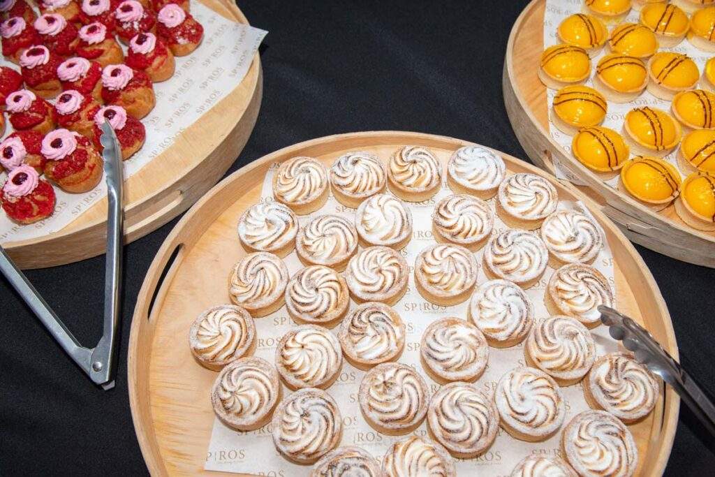 A close up of three platters of delicious colourful cakes and pastries, beautifully arranged on wooden serving boards.