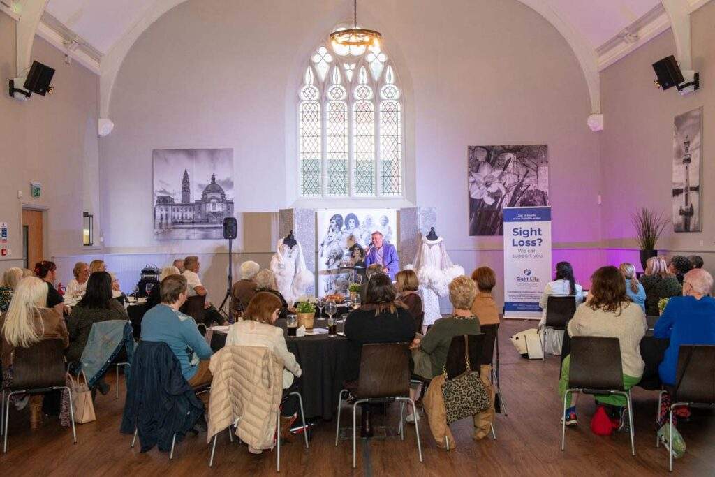 Guests seated around tables in Cornerstone's beautiful hall, listening to Ceri Dupree speaking on stage, surrounded by costumes and Sight Life branding.
