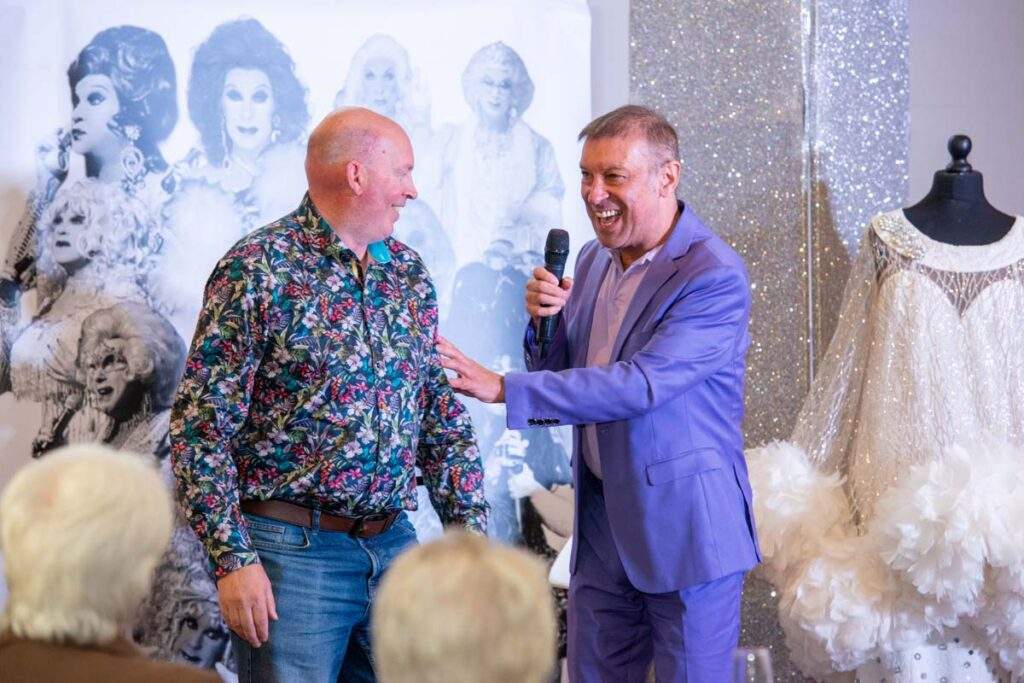Ceri, on stage and holding a microphone, laughing with another man who just volunteered to help him with a position to explain a story.