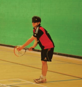 Picture of a member taking part in the VI (visually impared) tennis group, holding a racket and ball about to serve.