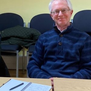 John sitting with a notebook and pen, smiling to camera