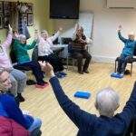 A group of people sat in chairs stretching at the Chair Yoga Group