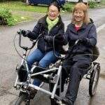 Two ladies sat on a Pedal Power bike.