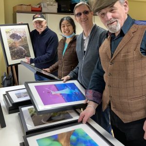 Four members of the photography group stood looking at framed images and smiling to camera