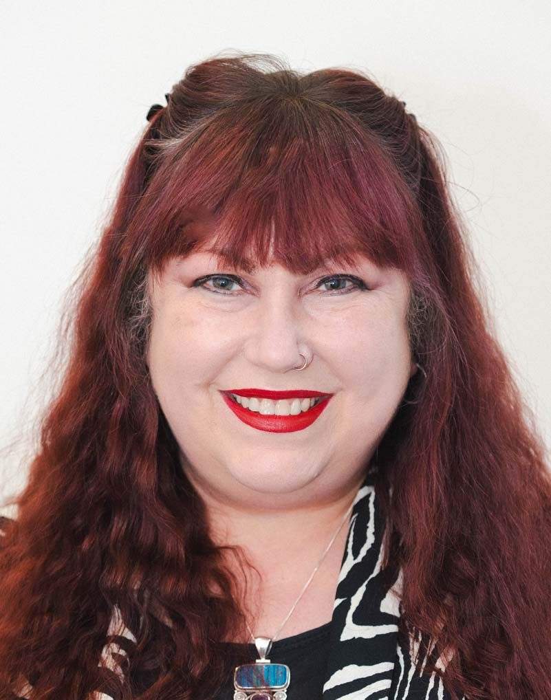 Head and shoulders photo of Valerie Baynton, smiling to camera. She has long reddy-brown hair and is wearing a black & white zebra print blouse.